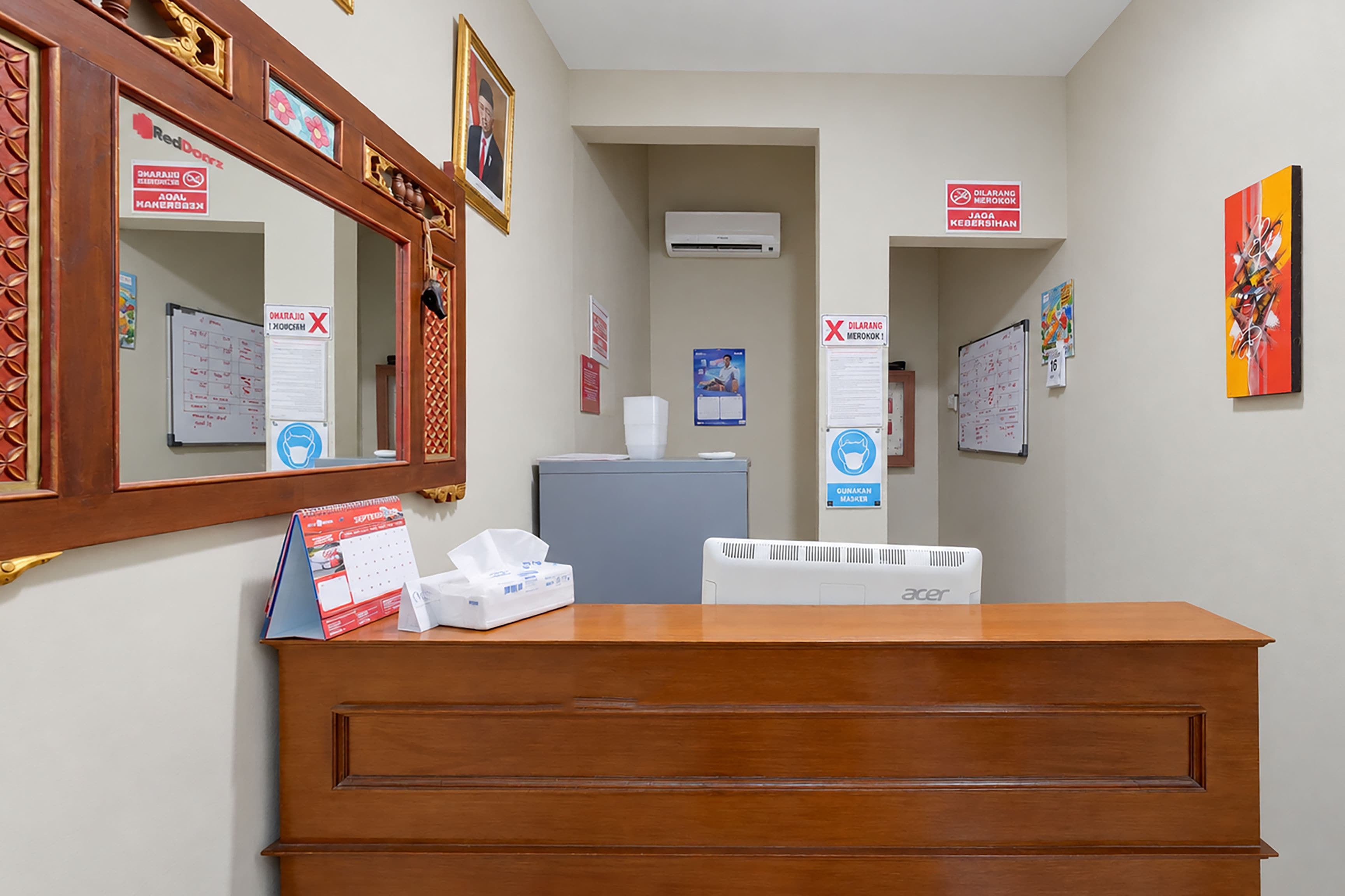 Un comptoir d’accueil avec un miroir, un calendrier, une boîte de mouchoirs et un panneau indiquant le port du masque.