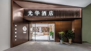 La entrada de un hotel de diseño moderno, con un letrero iluminado grande y un mostrador de recepción visible a través de las puertas de vidrio.