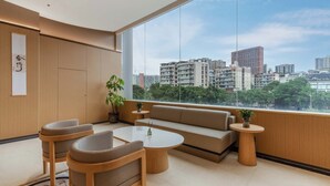 Una habitación moderna con un ventanal grande, un sofá, dos sillones, una mesita y una planta en maceta.