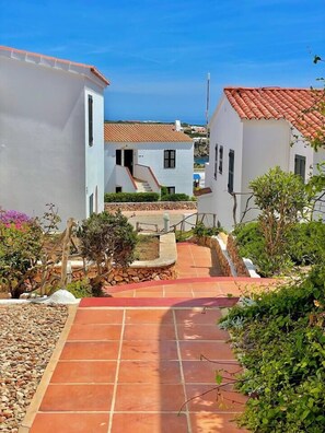 A residential area with white buildings, a red-tiled roof, and a paved walkway leading to a staircase. - Garbi: Newly Renovated Apartment with a Pool (S'Arenal D'En Castell (Menorca) (Urbanitzacio))
