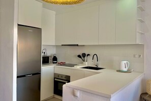 A modern kitchen with white cabinetry, a stainless steel refrigerator, a microwave, a kettle, and a sink with a faucet. - Garbi: Newly Renovated Apartment with a Pool (S'Arenal D'En Castell (Menorca) (Urbanitzacio))