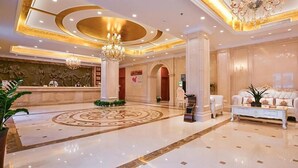 A hotel lobby with a reception desk, a chandelier, a patterned floor, and a seating area with a sofa and coffee table. - Vienna Hotel (Nanjing)