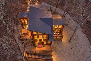 Une cabane en bois à plusieurs niveaux, dotée de nombreuses terrasses et de grandes fenêtres, et entourée d’arbres.
