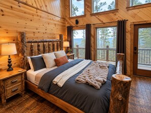 Ein Schlafzimmer einer Holzhütte mit einem großen Bett, zwei Nachttischen und Blick ins Freie.