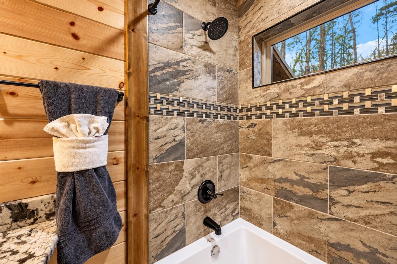 A bathroom with a shower, a bathtub, and a window with a view of trees.