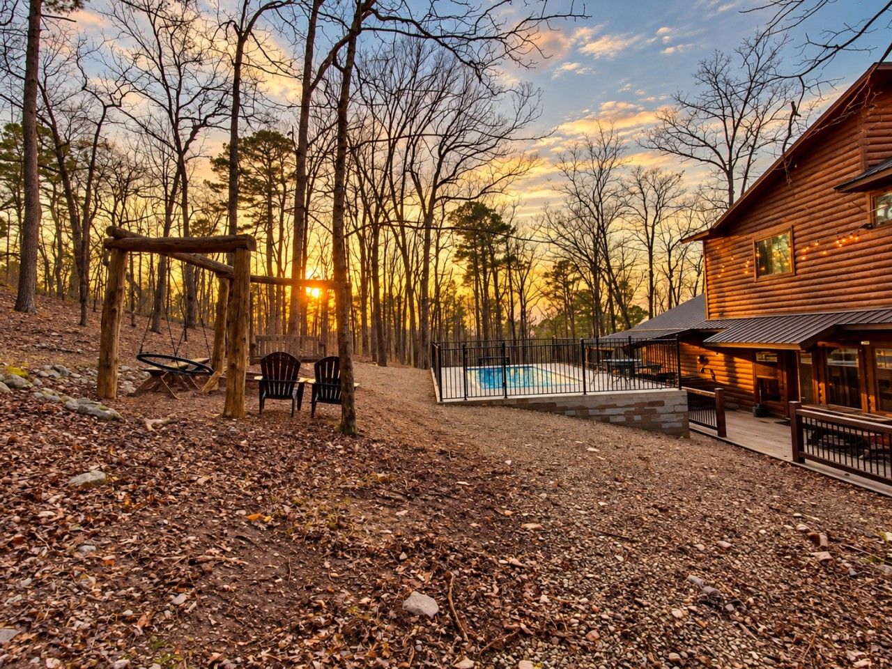A wooden cabin with a swimming pool, surrounded by trees and a deck area.