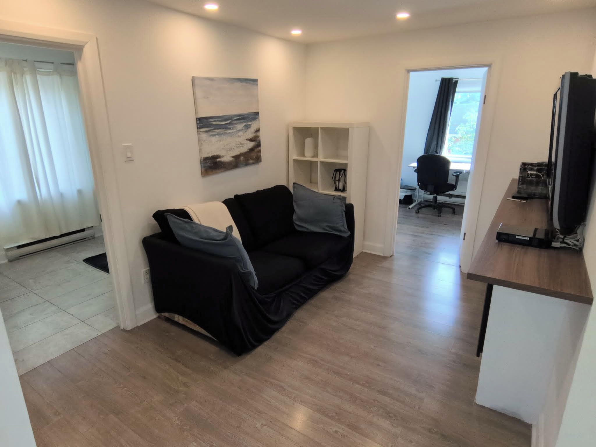 A modern living space with a black sofa, a painting, and a wooden floor.