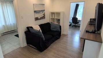 A modern living space with a black sofa, a painting, and a wooden floor.