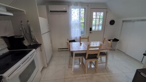 A compact kitchen with a dining table and chairs, a refrigerator, an oven, and a window with curtains.