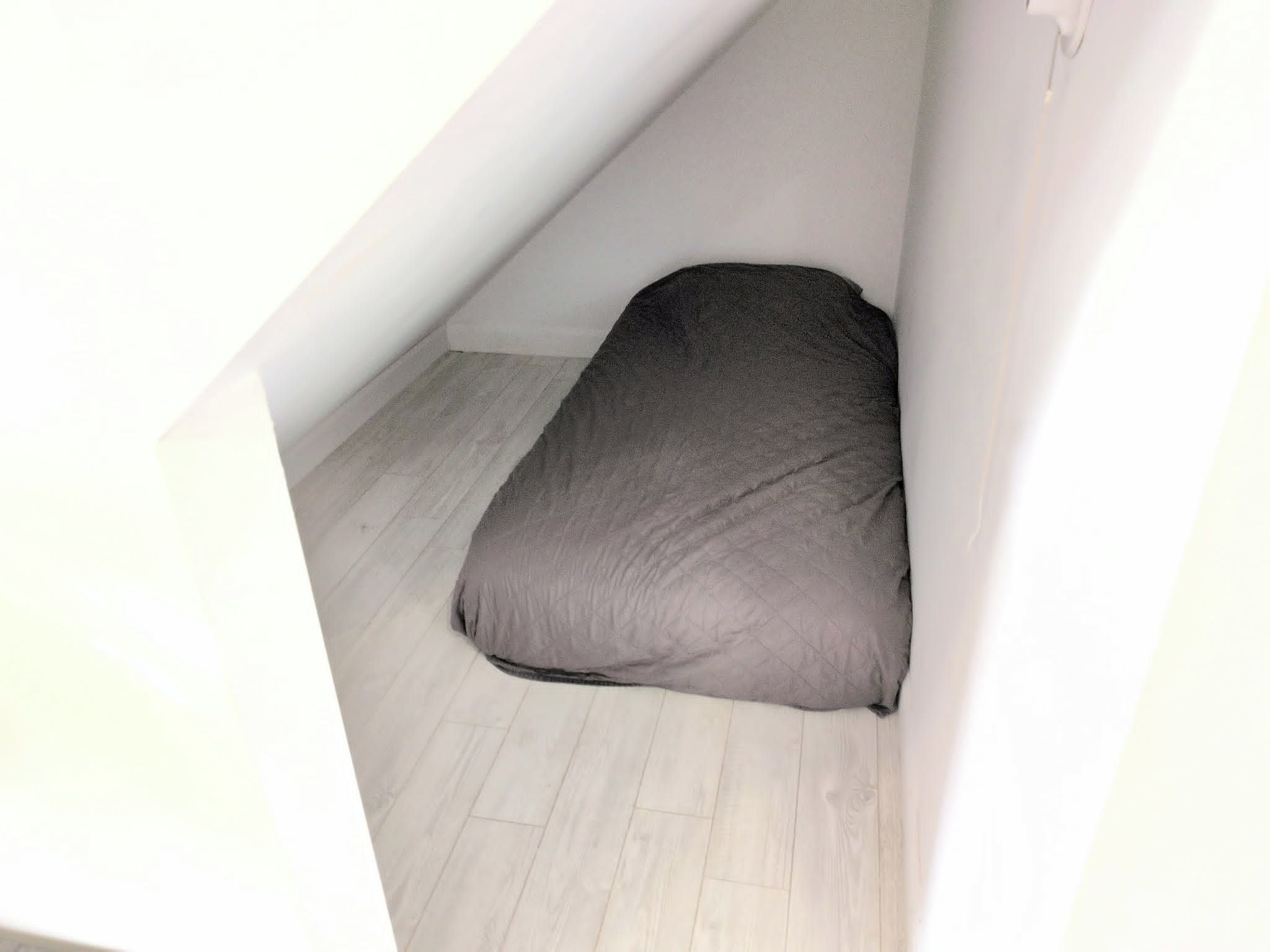 A small, enclosed attic space with a single mattress on a wooden floor.