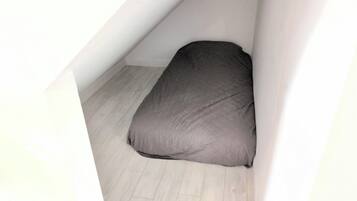 A small, enclosed attic space with a single mattress on a wooden floor.