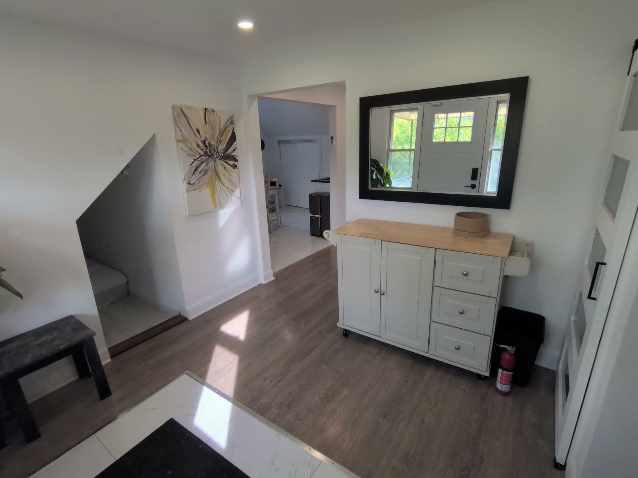Un vaste espace de vie avec un escalier, une cuisine dotée de meubles blancs et d’un plan de travail, et un grand miroir mural.