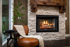 Ein Kamin aus Stein mit Feuer, ein Ledersessel mit Überwurfdecke und ein kleiner Tisch mit Tablett.