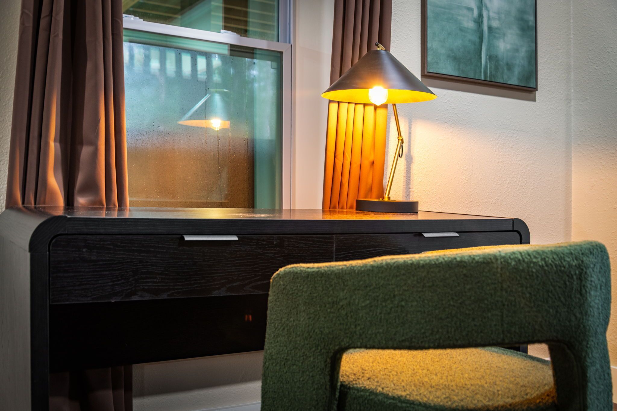 A desk with a lamp, a chair, and a window with curtains.