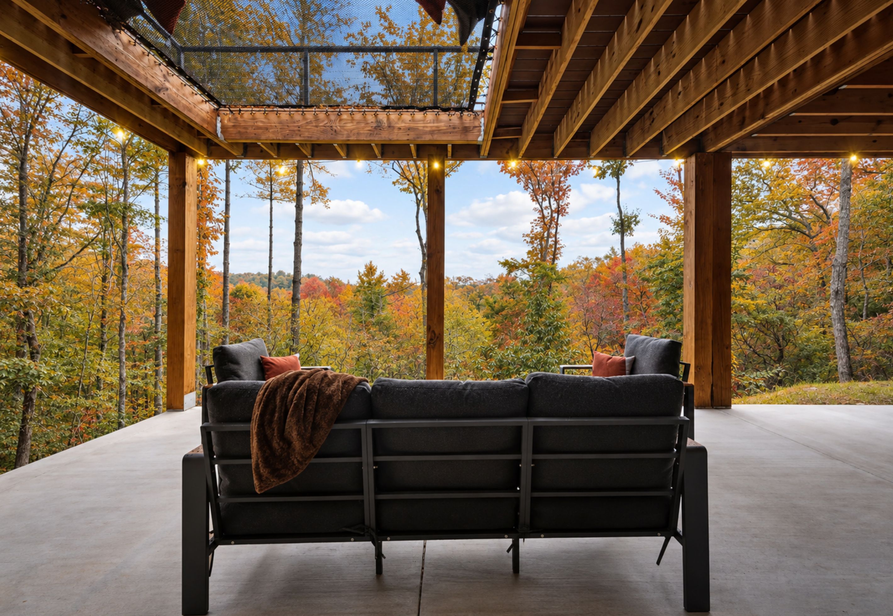 A covered outdoor seating area with a bench and cushions, overlooking a forested landscape.