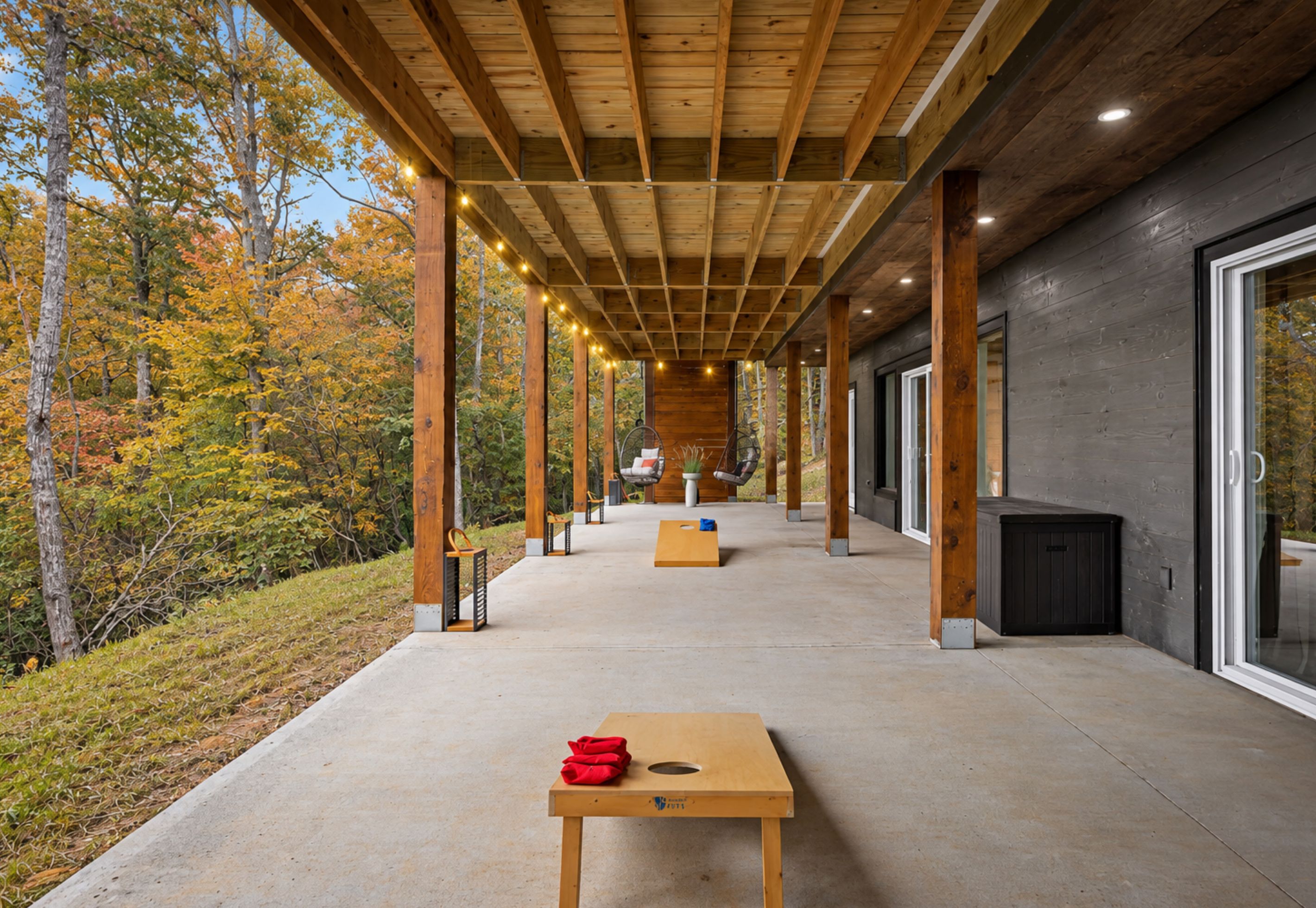 A covered outdoor area with a concrete floor, wooden beams, and a table with a red object on it.