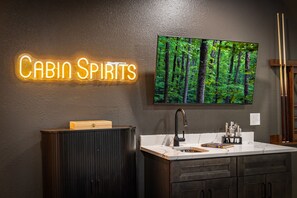 A modern bathroom with a neon sign reading 'CABIN SPIRITS,' a large mirror, a wooden cabinet, and a sink with toiletries. - Bluebird Reserve: Dome • Sauna • Hot-Tub • Cold Plunge • Fire-Pit • Putt • Views (Mineral Bluff)