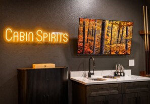 Ein modernes Badezimmer mit einem Neon-Schild mit der Aufschrift 'Cabin Spirits', einem Gemälde von Herbstlaub und einem Holzschrank.