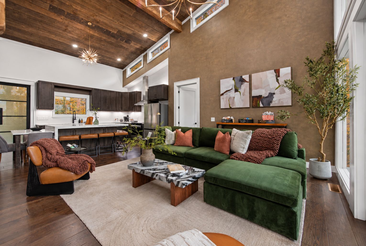 A spacious living area with a green sectional sofa, a coffee table, and a modern kitchen in the background.