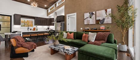 A spacious living area with a green sectional sofa, a coffee table, and a modern kitchen in the background.