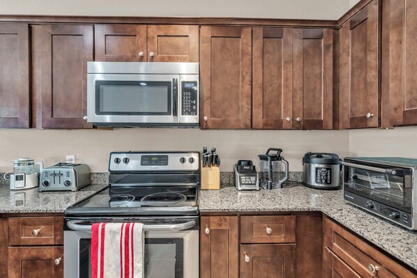 A kitchen with wooden cabinets, a stainless steel microwave, a stove, a toaster, and a coffee maker.