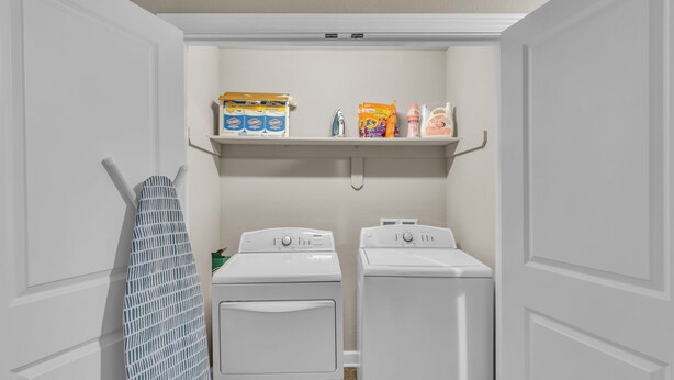 A laundry room with two white front-loading washers and dryers, a drying rack, and shelves above holding laundry supplies.