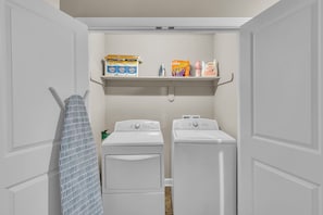 A laundry room with two white front-loading washers and dryers, a drying rack, and shelves above holding laundry supplies. - Perfect 2-bedroom ranch home 12mins to KCAirport & 5min to StLuke North Hospital (Kansas City)