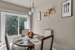 Un coin repas avec une table ronde, des chaises, un vase de fleurs et des œuvres d’art encadrées accrochées aux murs.