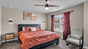 A bedroom with a bed, a chair, a ceiling fan, and a window with curtains.