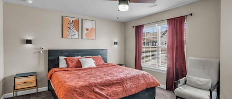 A bedroom with a bed, a chair, a ceiling fan, and a window with curtains.