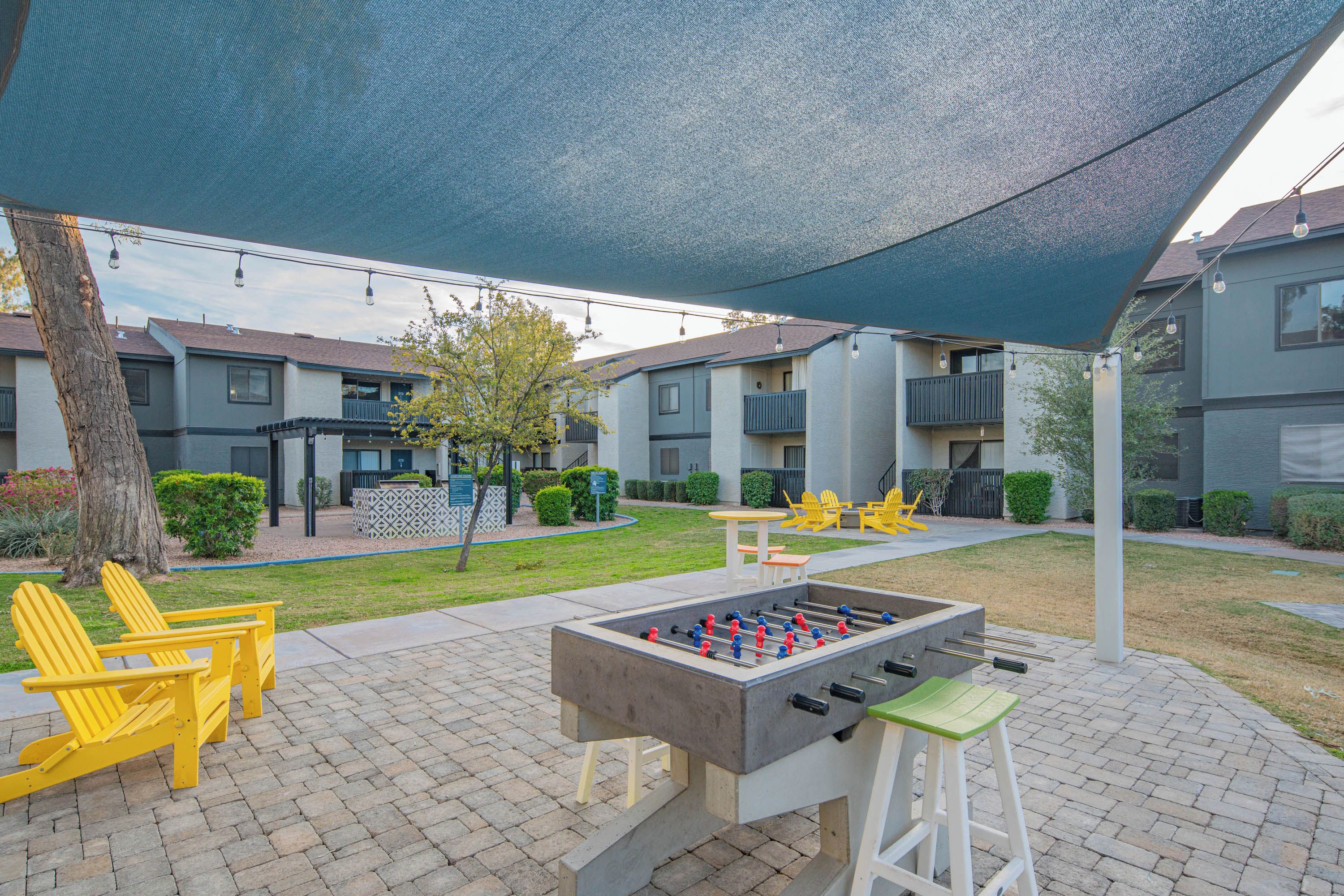 Un espace extérieur aménagé en terrasse, avec une table de baby-foot, des fauteuils Adirondack jaunes et un coin salon abrité.