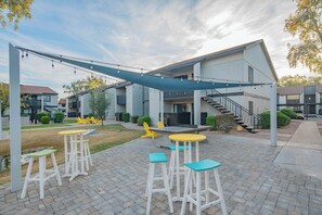 Un patio exterior con una zona de estar cubierta, una escalera que conduce a un nivel superior y vistas de edificios cercanos.
