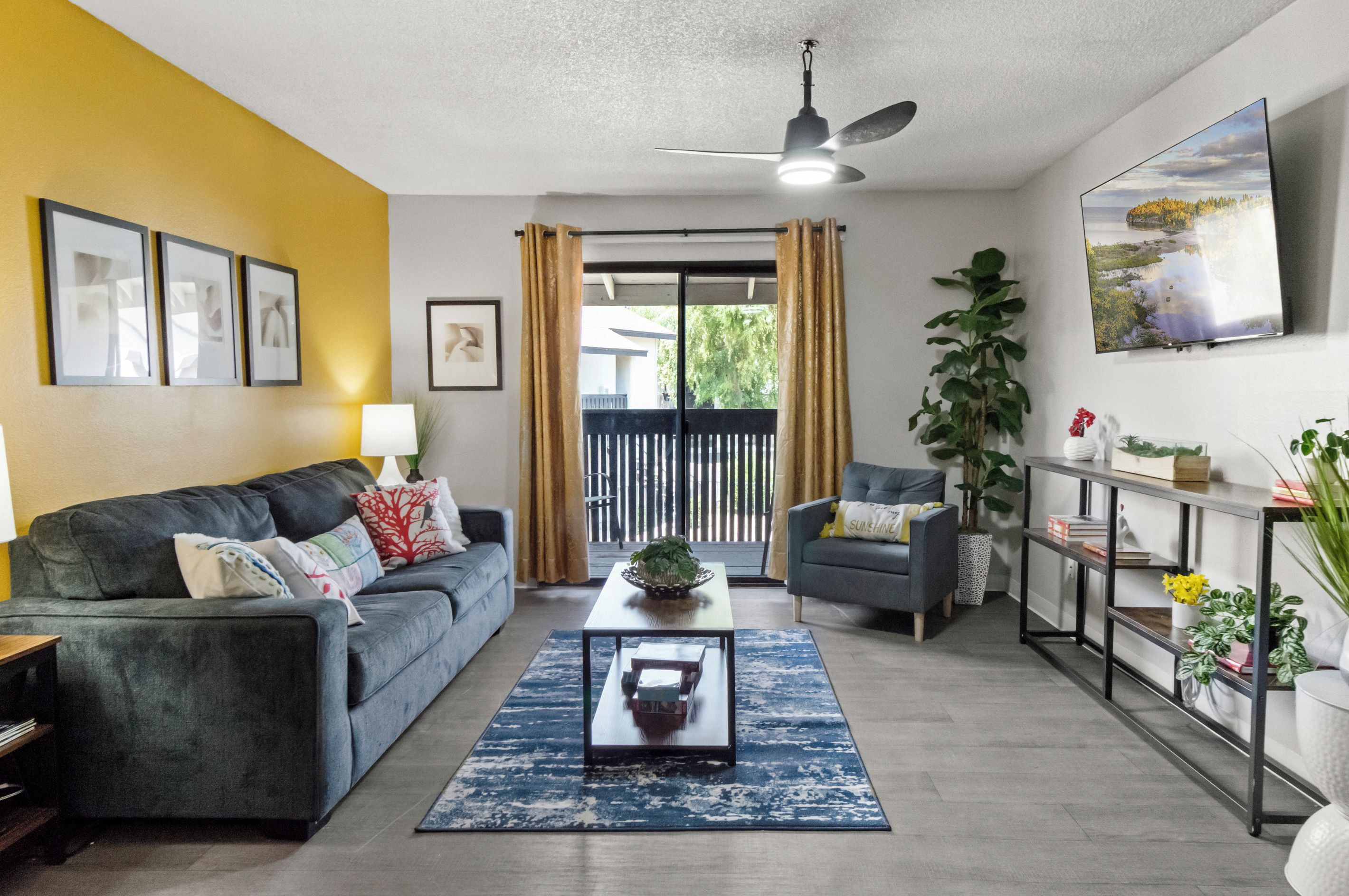 Sala de estar com sofá, poltrona, mesa de centro e vista para o exterior através de uma porta de correr.