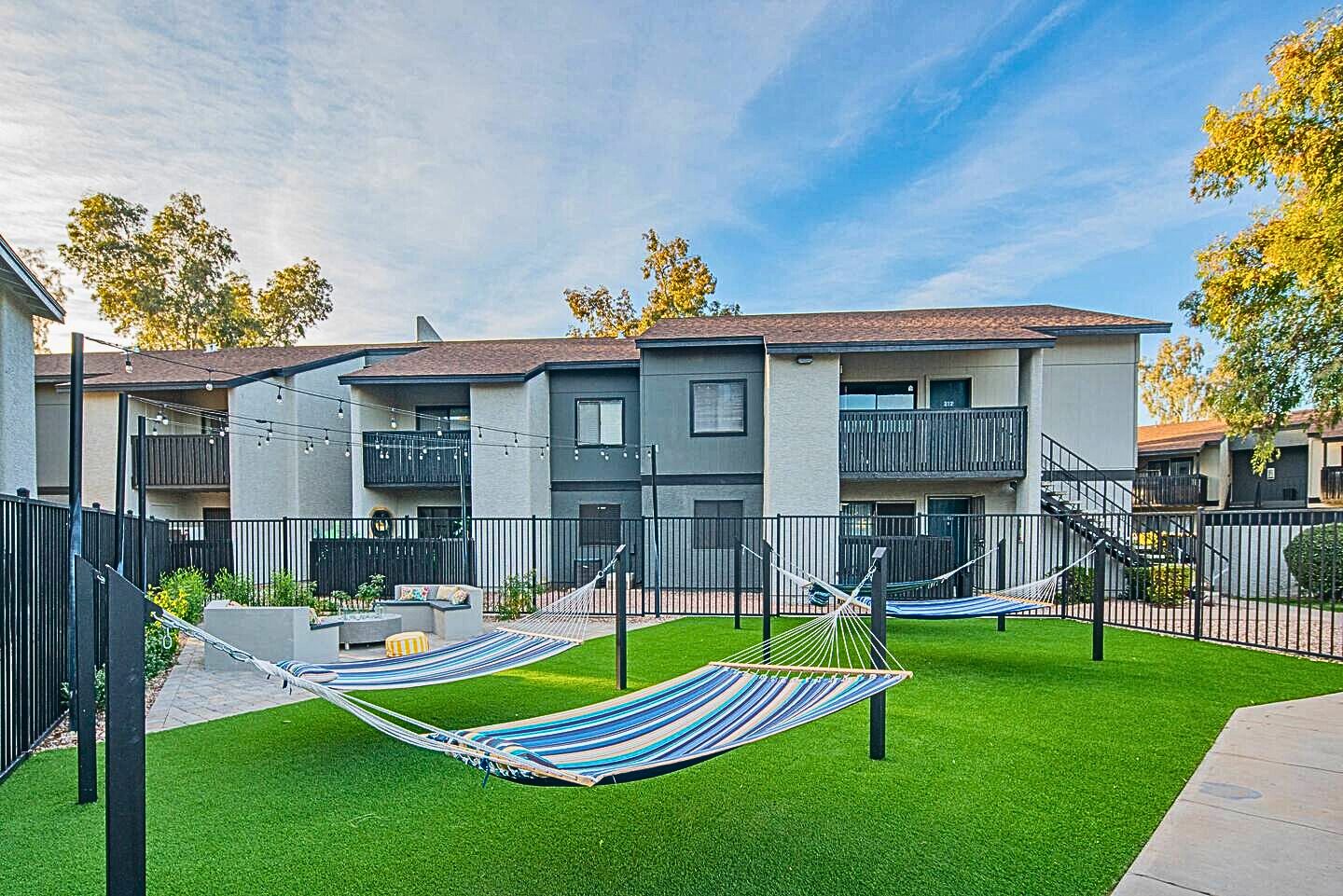 A modern apartment complex with a well-maintained lawn, two hammocks, and a balcony.