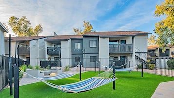 A modern apartment complex with a well-maintained lawn, two hammocks, and a balcony.