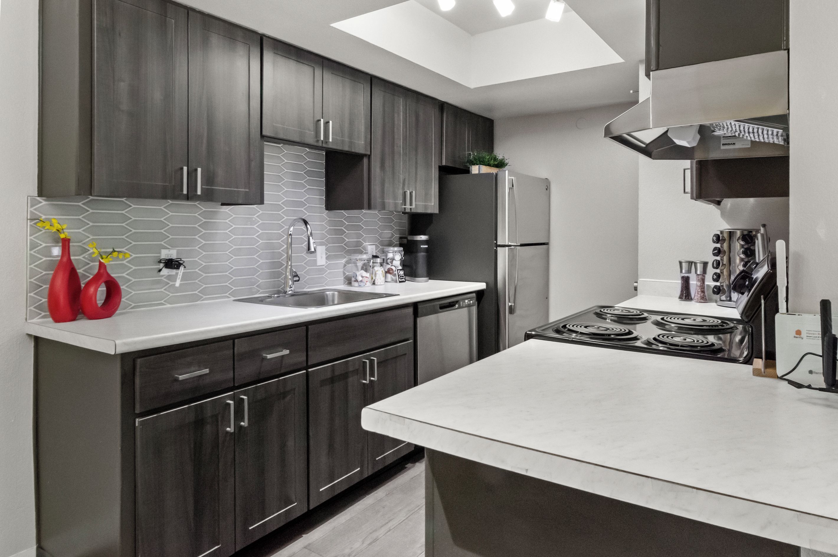 A modern kitchen with dark cabinets, a white countertop, and stainless steel appliances.