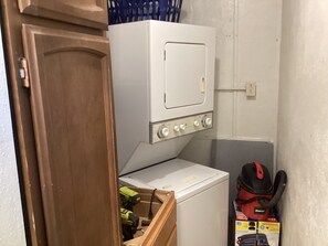 Ein Waschraum mit einer weißen Waschmaschine und einem Trockner, einer Holztür und einer Werkzeugkiste mit Werkzeugen.
