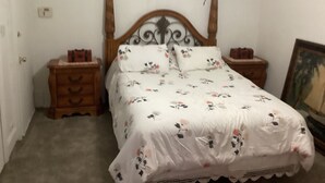 Une chambre à coucher avec un lit à baldaquin en bois, une literie à motifs floraux, deux tables de chevet et un tableau encadré au mur.