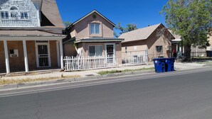 Une rue résidentielle bordée de maisons, avec une clôture blanche et une benne à ordures bleue.