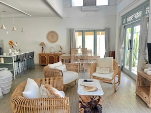 A spacious living area with wicker furniture, a dining table, and a kitchen area with bar stools. - Stylish 3BR Villa with Large Pool Central Seminyak (BADUNG)