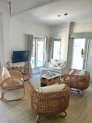 A spacious living room with wicker furniture, a flat-screen TV, and a balcony with curtains. - Stylish 3BR Villa with Large Pool Central Seminyak (BADUNG)
