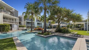 Un hotel con piscina, palmeras y césped cuidado.