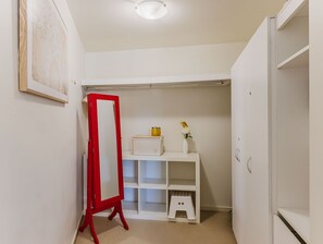 Ein weißer Kleiderschrank mit Regalen, ein Spiegel mit rotem Rahmen und ein kleiner Hocker.
