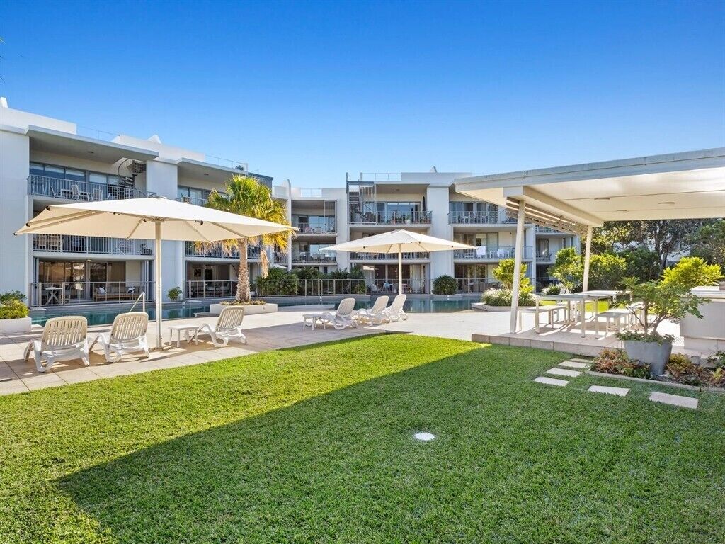 A modern hotel with outdoor seating areas, a swimming pool, and a well-maintained lawn.
