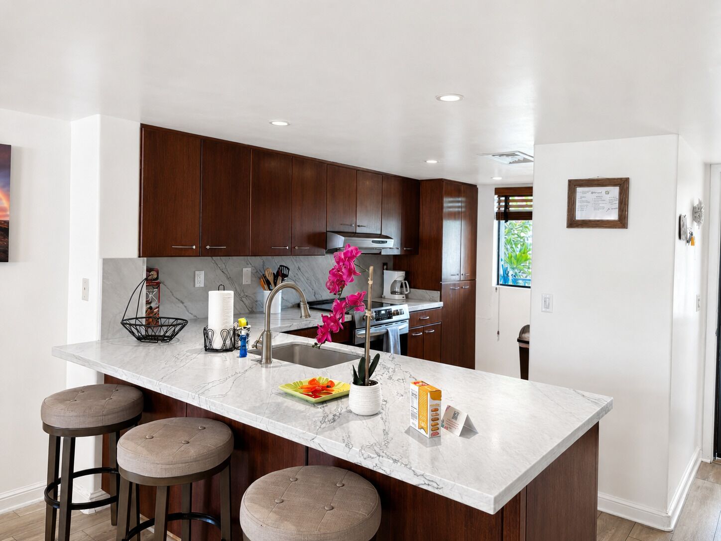 Una cocina moderna con alacenas de madera oscura, encimera de mármol y una isla central con taburetes.