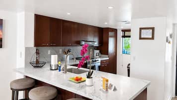 Una cocina moderna con alacenas de madera oscura, encimera de mármol y una isla central con taburetes.