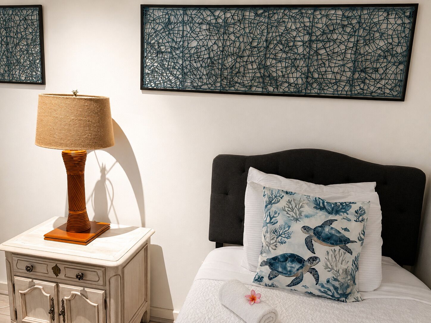 Un dormitorio con una cama, una mesita de noche, una lámpara y dos obras de arte en la pared.