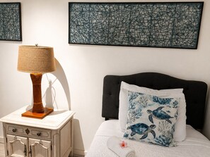 A bedroom with a bed, a nightstand, a lamp, and two wall art pieces. - Luxury Oceanfront Escape. Ocean Views, Walk to Beach, Snorkel, Pool, Spa, AC (Kailua Kona)