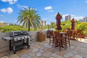 Une terrasse extérieure avec un barbecue, des chaises en bois et des parasols.