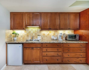 A kitchen with wooden cabinets, a granite countertop, a built-in microwave, and a dishwasher. - Charming Waikiki Studio, Kitchenette+Walk to Beach (Honolulu)